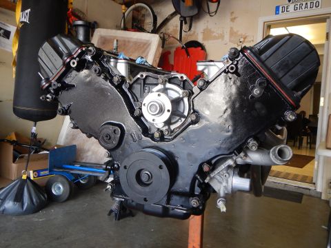 2003 Ford Crown Victoria - Front of an assembled V8 engine on a stand in a garage, showing the black timing cover, water pump, and pulleys.