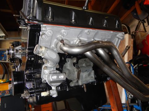 2003 Ford Crown Victoria - Side view of a V8 engine on a stand with tubular headers, accessory pulleys, and raw aluminum block castings.