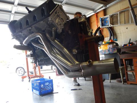 2003 Ford Crown Victoria - Low garage shot of a V8 engine on a stand showing long-tube headers merging into collector pipes, person behind.