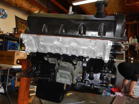 2003 Ford Crown Victoria - assembled V8 long block resting on a stand in a garage, black valve cover above a bare aluminum intake face.