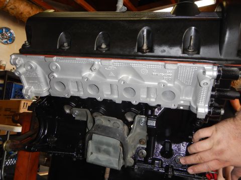 2003 Ford Crown Victoria - Side of a V8 engine with cast aluminum intake face, a metal mounting bracket, and a hand resting at the block edge.