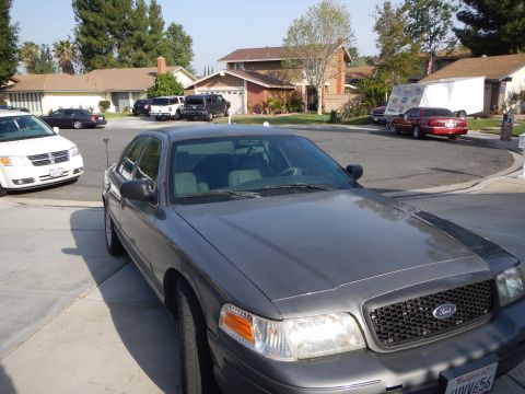 2003 Ford Crown Victoria - Front of a gray Ford sedan showing the Ford oval grille badge, parked in a suburban cul-de-sac driveway.