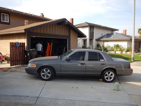 2003 Ford Crown Victoria - gray Ford Crown Victoria sedan in profile parked on a driveway in front of an open residential garage.