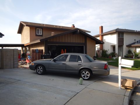 2003 Ford Crown Victoria - gray Ford sedan parked in the driveway of a two-story suburban home with an open garage and bikes nearby.