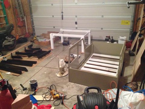 2005 Jeep Wrangler - A cluttered garage contains unassembled furniture pieces, a motorcycle, and various tools, suggesting a DIY project.