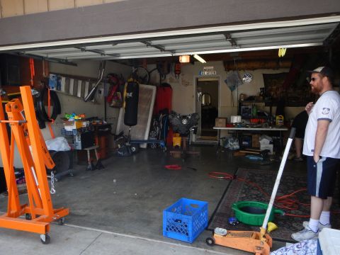 2003 Ford Crown Victoria - cluttered home garage interior showing an orange engine hoist, a heavy punching bag, scattered tools, and a man standing at the right.