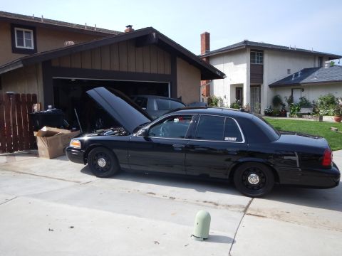 2003 Ford Crown Victoria - black Ford Crown Victoria sedan with steel wheels and its hood raised sits in a residential driveway in front of a garage.