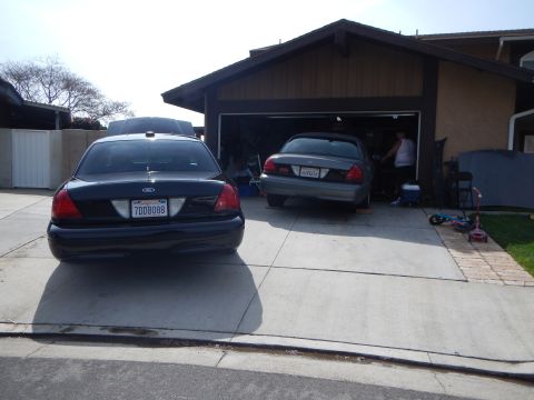 2003 Ford Crown Victoria - black Ford sedan (plate 7DDB088) and a gray Ford sedan are parked in a residential driveway in front of an open garage.