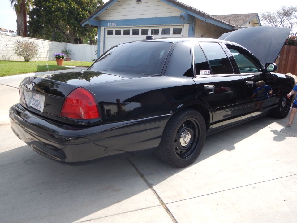 Black Ford Crown Victoria with steel wheels and open hood in a driveway