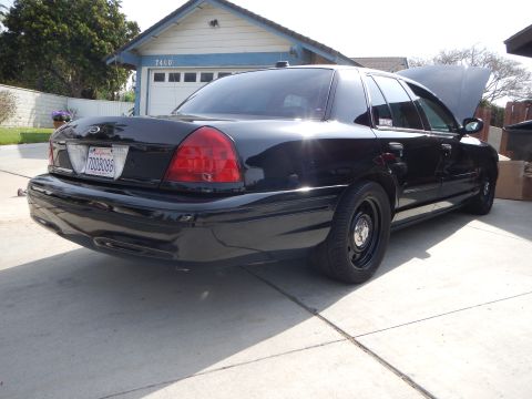 2003 Ford Crown Victoria - Rear view of a black Ford Crown Victoria sedan with steel wheels and an open hood parked in a residential driveway, plate visible.