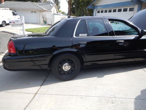 2003 Ford Crown Victoria - Side profile of a black Ford Crown Victoria sedan with black steel wheels and a window decal, parked in a residential driveway.