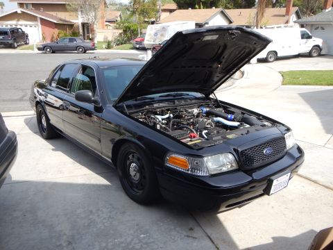 2003 Ford Crown Victoria - black Ford Crown Victoria sedan sits in a driveway with its hood open, revealing a modified engine bay with blue intake piping.