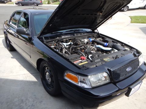 2003 Ford Crown Victoria - Front three-quarter view of a black Ford Crown Victoria with its hood up, showing a modified engine bay with blue intake piping.