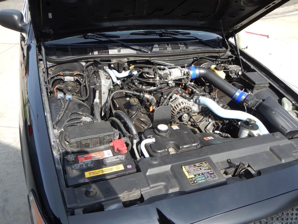 Engine bay of a Ford sedan with modified intake, blue piping, and red battery cap