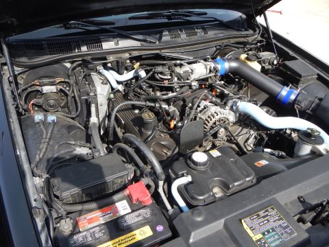 2003 Ford Crown Victoria - Engine bay showing an alternator, battery, and blue aftermarket intake piping with the hood open.