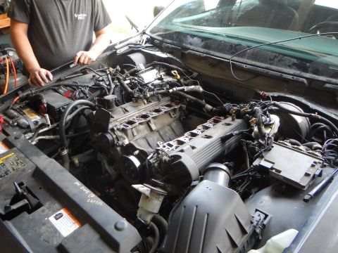 2003 Ford Crown Victoria - partially disassembled engine in a vehicle bay with intake removed and exposed cylinder heads, a person standing alongside.