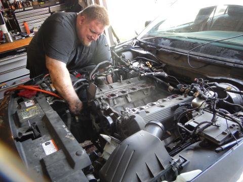 2003 Ford Crown Victoria - man leans over the engine bay of a vehicle, working on a disassembled engine with exposed cylinder heads.