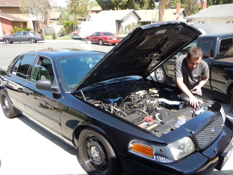 2003 Ford Crown Victoria - black Ford Crown Victoria sedan sits with its hood up as a man reaches into the engine bay in a driveway.