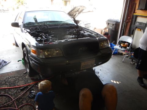 2003 Ford Crown Victoria - silver Ford Crown Victoria sedan with open hood in a garage as a person works under it and a toddler watches.