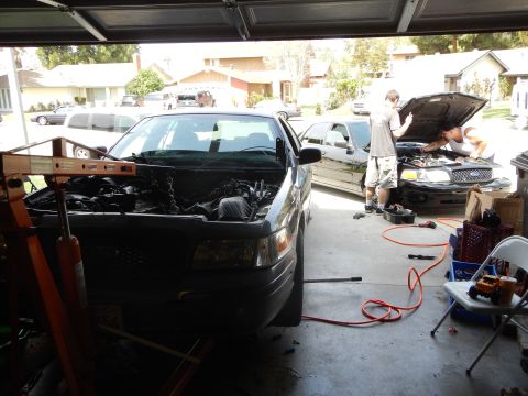 2003 Ford Crown Victoria - gray Ford sedan is mid engine work inside a garage while a person works on another vehicle out in the driveway.