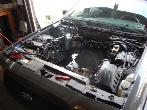 2003 Ford Crown Victoria - engine bay of a gray Ford sedan sits empty after engine removal, with hoses and the Ford-emblem grille in view.