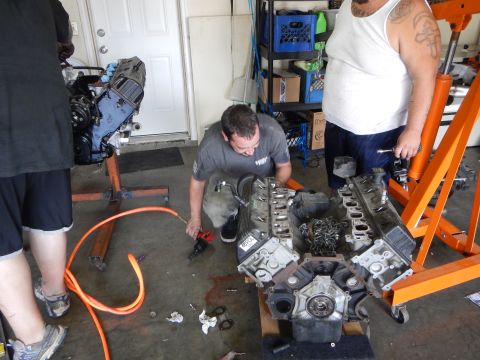 2003 Ford Crown Victoria - man works on a disassembled V8 engine block on the garage floor while another man stands nearby with tools.