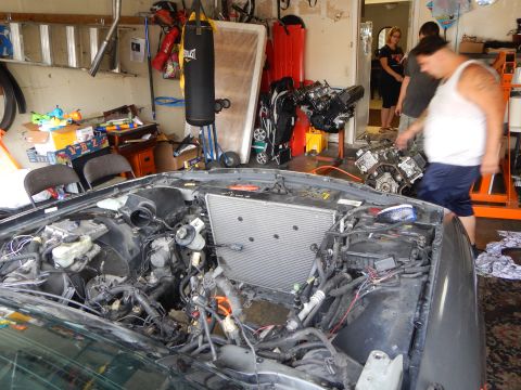 2003 Ford Crown Victoria - gray sedan sits with its front clip and engine removed, exposing the radiator and wiring harness, as a man walks past in a garage.