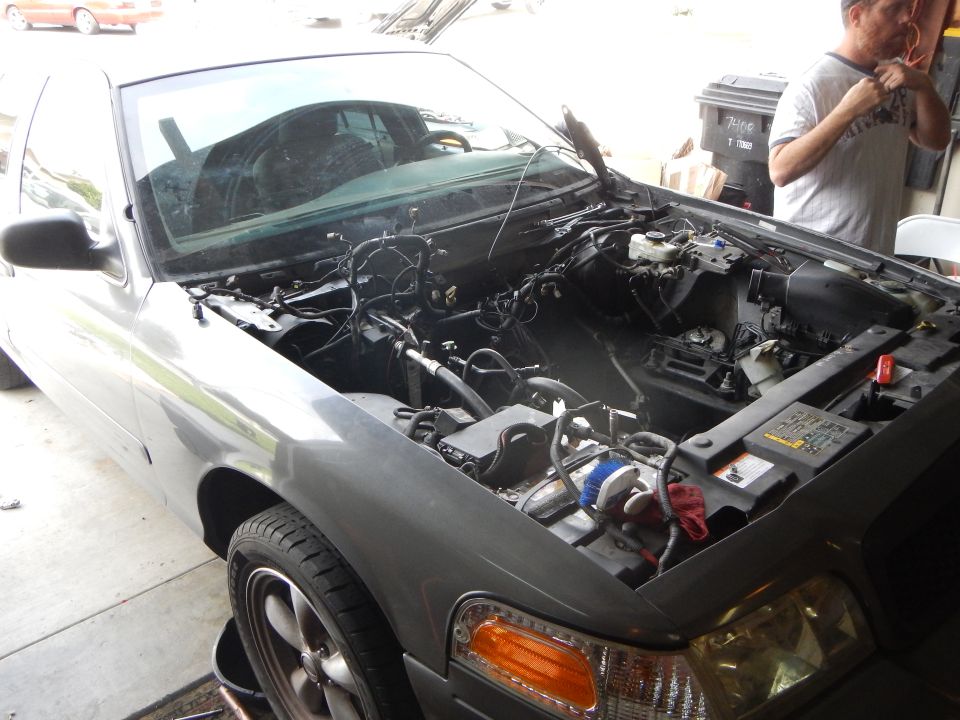 Gray sedan with hood up and engine removed, exposing empty engine bay and wiring