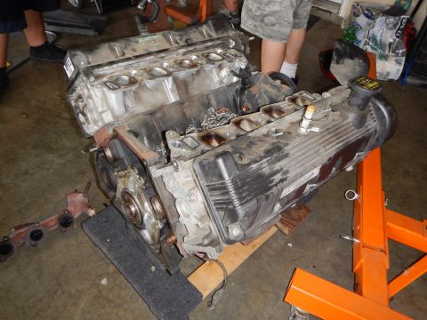 2003 Ford Crown Victoria - disassembled V8 engine sits on a stand with cylinder heads and intake ports exposed and an exhaust manifold on the floor.