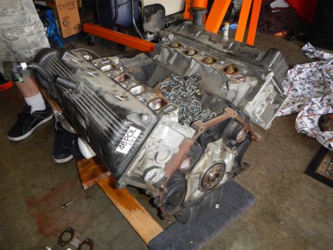 2003 Ford Crown Victoria - V8 engine block marked 46POL sits on the floor with cylinder heads off, timing chains and front cover exposed.