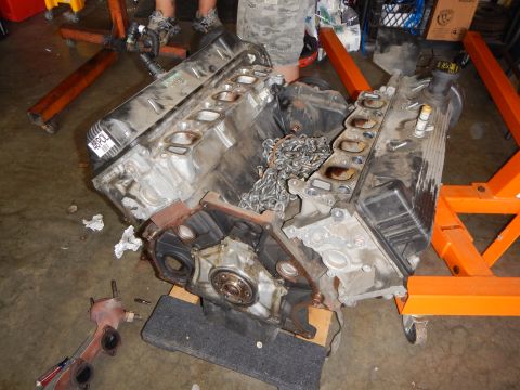 2003 Ford Crown Victoria - open V8 engine block rests on the floor with its cylinder heads, intake ports and timing chains exposed for rebuild.