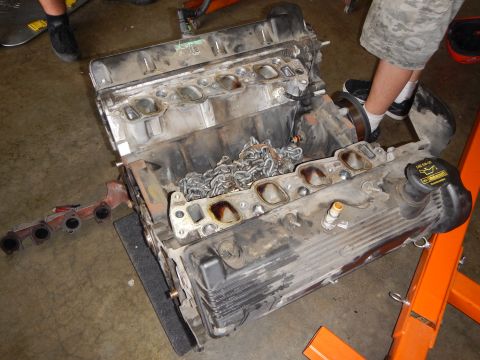 2003 Ford Crown Victoria - V8 engine with cylinder heads removed shows the combustion chambers and timing chains, an exhaust manifold lying nearby.