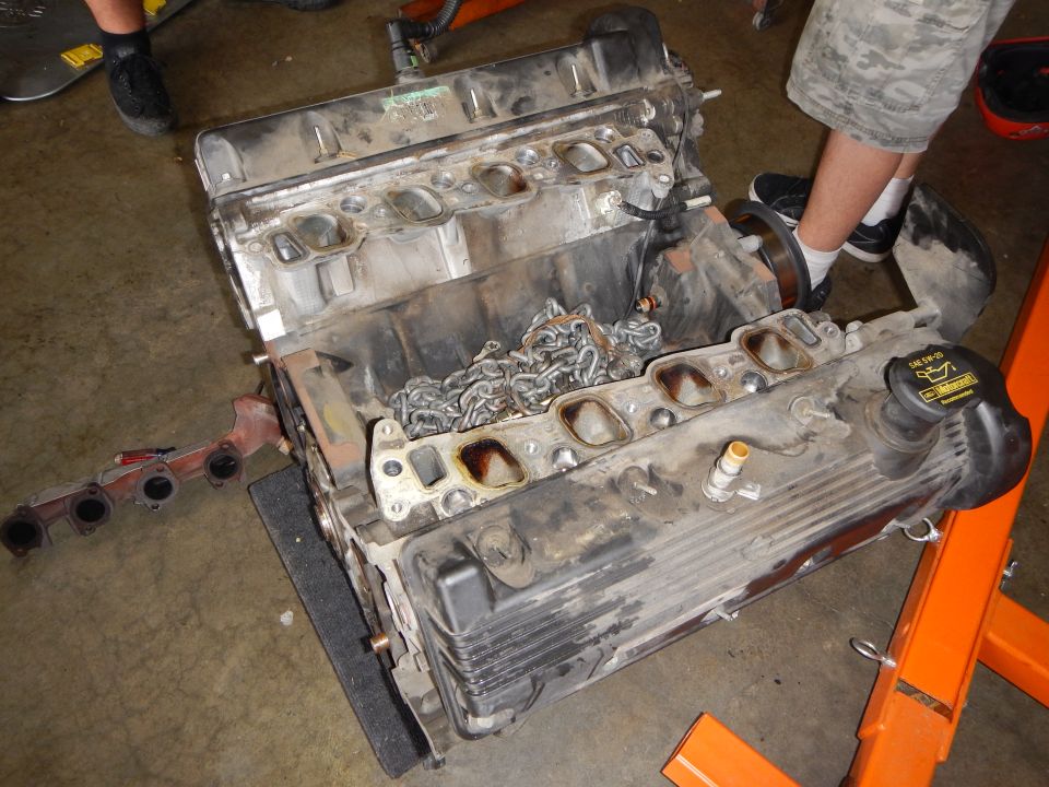 V8 engine with heads removed showing combustion chambers and timing chains on garage floor
