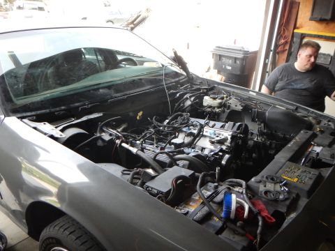 2003 Ford Crown Victoria - gray Ford sedan with its hood up in a garage shows a bare engine bay while a man stands at the right.