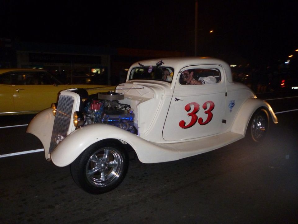 White hot rod coupe with exposed engine and red number 33 on door, driving at night