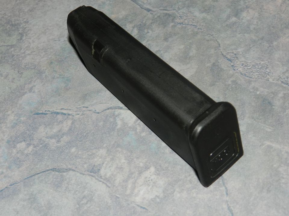 Black gun magazine with "GLOCK" logo on the base, resting on a gray, marbled surface