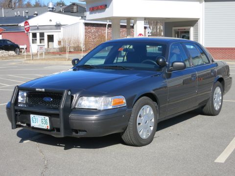 2001 Ford Crown Victoria - A dark grey 2001 Ford Crown Victoria, equipped with a push bar, is parked in a lot.