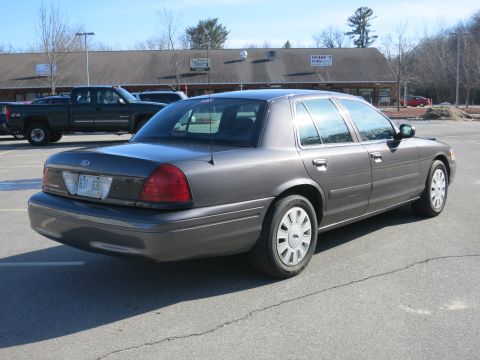 2001 Ford Crown Victoria - A gray 2001 Ford Crown Victoria is parked in a lot with other vehicles and a building in the background.