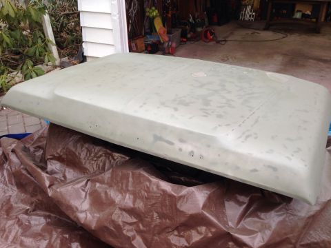 1979 Ford Bronco - A car hood, prepped for paint, sits on a brown tarp in front of a garage.