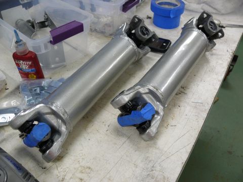 Two silver driveshafts with blue tape on U-joints, on a workbench with Loctite