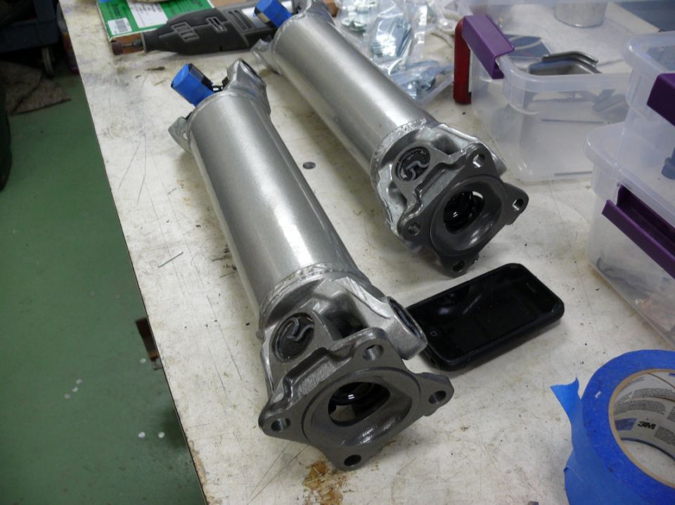 Two driveshafts with blue caps on a workbench, next to a phone and tape