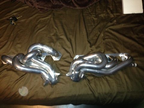 1992 Ford F-150 - Two chrome exhaust headers are laid out on a brown, textured surface, possibly a bedspread.