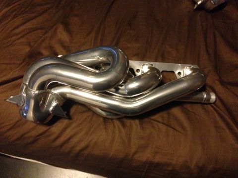 1992 Ford F-150 - A set of polished exhaust headers rests on a brown fabric surface, with a website URL visible at the bottom.