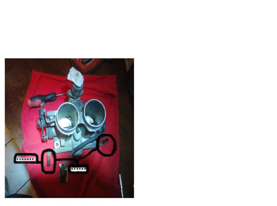 Throttle body with two openings, a screwdriver, and handwritten labels 'CLOGGED' and 'RUSTED'