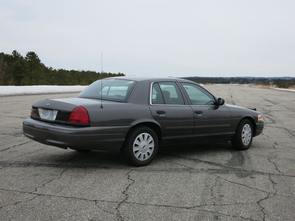 Dark grey 2001 Ford Crown Victoria sedan, rear quarter view, parked on cracked asphalt
