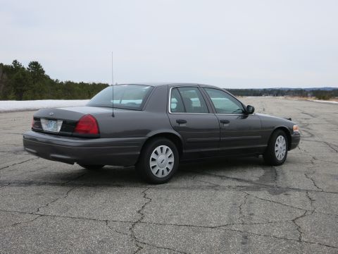 2001 Ford Crown Victoria - A dark grey 2001 Ford Crown Victoria sedan is shown from the rear three-quarter angle on a paved surface with trees in the background.