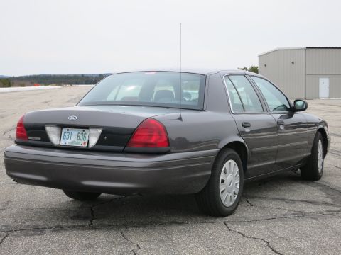 2001 Ford Crown Victoria - This dark grey Ford Crown Victoria is parked on cracked asphalt with a building in the background.