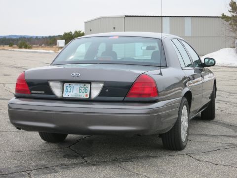 2001 Ford Crown Victoria - Rear view of a dark grey 2001 Ford Crown Victoria parked on cracked asphalt.