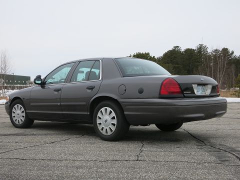 2001 Ford Crown Victoria - A dark grey 2001 Ford Crown Victoria sedan is viewed from the rear three-quarter angle on a cloudy day.