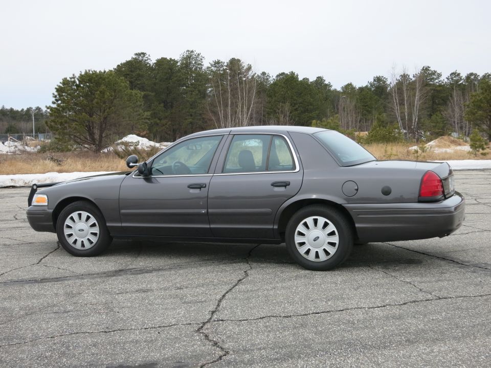 Side view of a grey 2001 Ford Crown Victoria parked on cracked asphalt